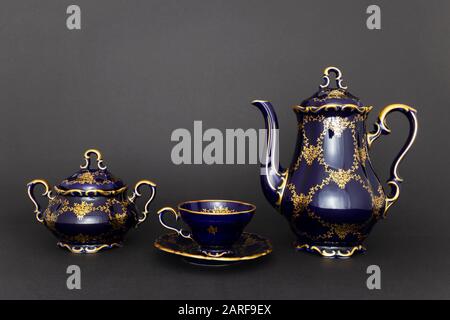 Closeup of a beautiful cobalt blue colored vintage porcelain tea set with golden floral pattern on dark gray background. The set includes a tea pot, a Stock Photo