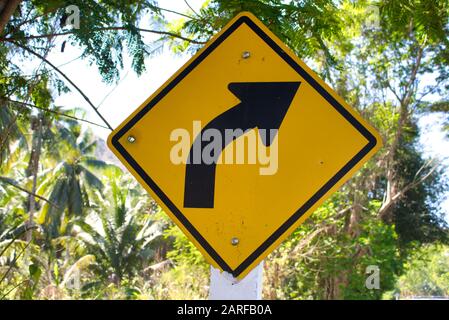 This unique photo shows a road sign on a road in Thailand showing a right turn. The label is yellow and the arrow is black! Stock Photo