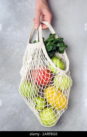 Zero Waste Eco Mesh Shopping Bag With Fruits Vegetables Greens On Grey Concrete Background. Hand Holding Eco Friendly Bag Stock Photo