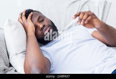 Sick african guy lying on sofa and checking his temperature Stock Photo
