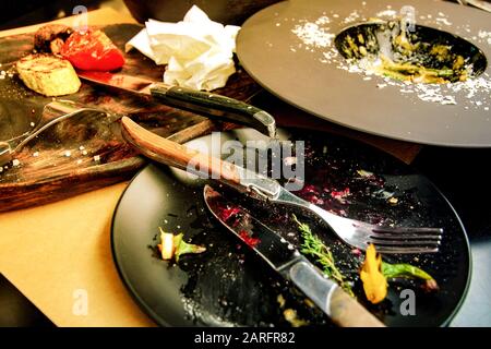 Table in restaurant with leftover food on black plates Stock Photo