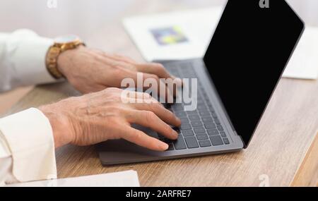 Unrecognizable Senior Man Using Laptop Typing Sitting At Workplace, Closeup Stock Photo
