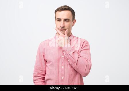 Pensive caucasian young man thinking or considering idea, looking at free copy space aside. Thoughtful millennial male client touch chin making decisi Stock Photo