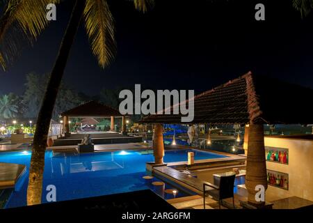 Night view of tropical pool surrounded by palm trees and lounge chairs Stock Photo
