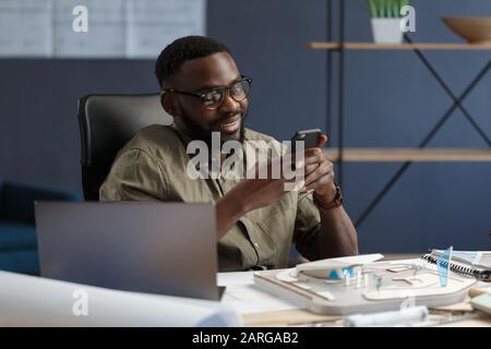 Young Afro-American man using smartphone and smiling. Happy businessman using mobile phone apps, texting message, browsing internet, looking at Stock Photo