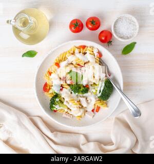 Pasta fusilli with vegetables, boiled steamed meat, white sauce on white wooden table, low-calorie food, low-fat diet, top view Stock Photo