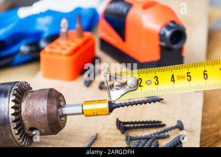 A steel screw is placed on an electric drill on a wooden board background. The concept of tools and repair work. Steel screws. Metal screw Stock Photo