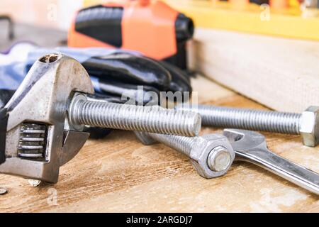 An adjustable spanner lies near the bolts and nuts of the washer against the background of wooden boards. The concept of tools and repair work. Stock Photo