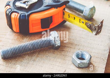Steel bolts and nuts lie on wooden boards next to a tape measure ruler. The concept of tools and repair work. Stock Photo