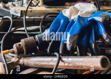 An electric drill and blue gloves lie on a pile of cable and hammers. Tools for the job. Stock Photo