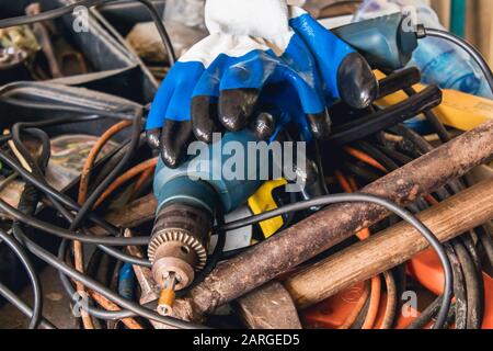 An electric drill and blue gloves lie on a pile of cable and hammers. Tools for the job. Stock Photo