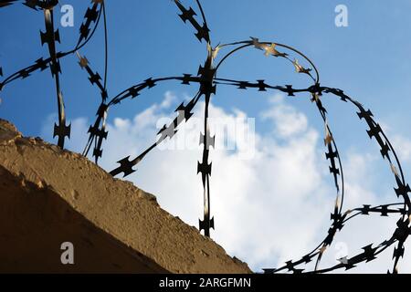 Concrete fence topped with razor wire against blue sky Stock Photo