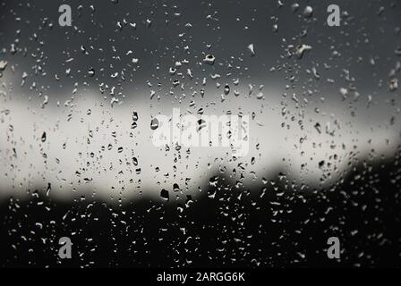 Raindrops on the window pane. Black, gray, white gradient on blurry background. Cloudy rainy weather outside the window. Cooling, raining, bad weather Stock Photo