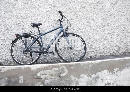 Dark gray bicycle stands leaning against white plastered wall with rough surface Stock Photo
