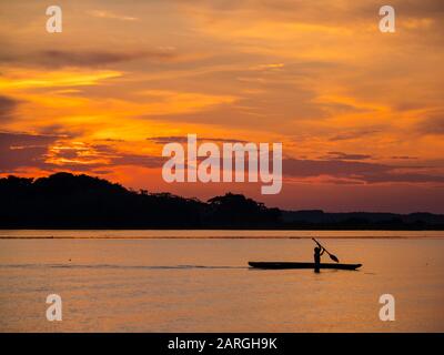 Young man paddling his fishing boat at sunset over calm waters on Clavero Lake, Amazon Basin, Peru, South America Stock Photo