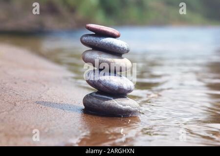 Stack of balancing pebble stones on sand and water edge. Zen symbol against blurred nature background. Stock Photo