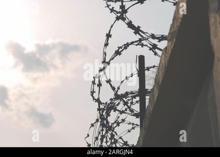 Barbed wire over a concrete fence against gray cloudy sky Stock Photo
