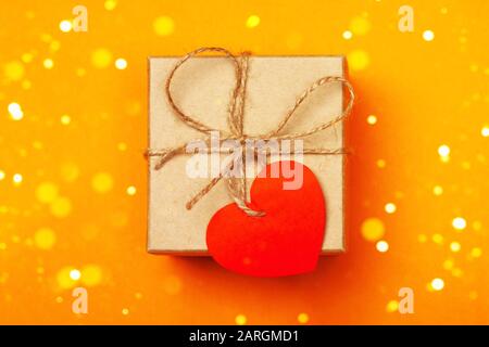 A gift with cute heart on the orange background. Surprise your loved one. The concept of the St. Valentine's day, birthday and other holidays. Zero waste. Flat lay Stock Photo