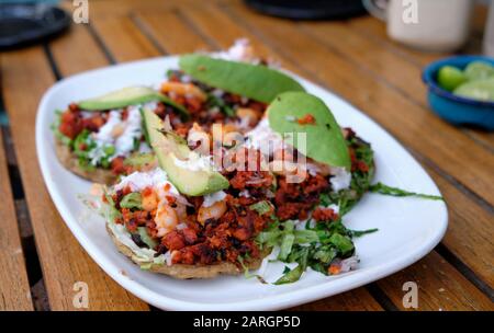 Mexican tostada with topping of minced sausage and shrimp, with avocado on top, on a white plate Stock Photo