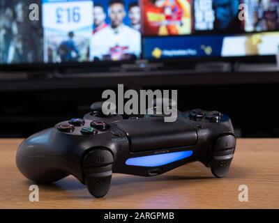 UK, Jan 2020: Sony dualshock remote controller wireless for Playstation 4 in front of online store on television screen