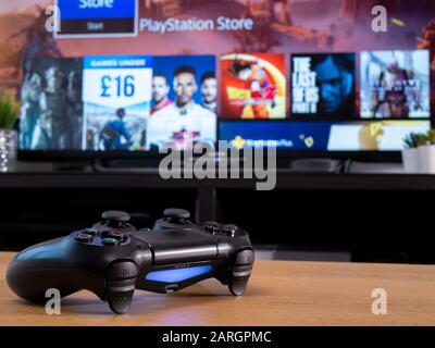 UK, Jan 2020: Sony Dualshock 4 wireless controller with Playstation online store on television screen behind