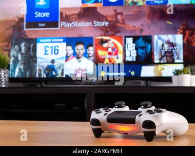 UK, Jan 2020: White Sony Dualshock 4 controller for PS4 with online store on television screen behind