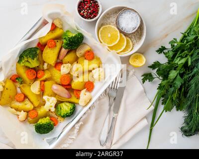 Roasted vegetables on tray with parchment on marble table. Potatoes, carrots, broccoli cauliflower and onions. Top view Stock Photo