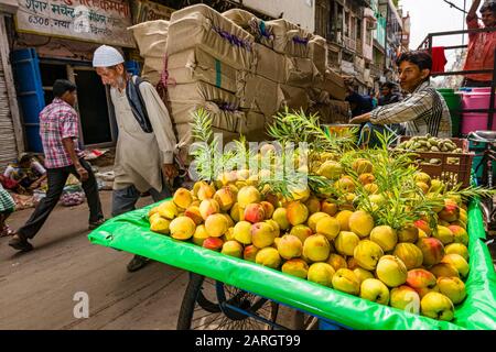 Goods and big loads get transported by human power on carts on Khari Baoli Road in Old Delhi, street vendor selling peaches Stock Photo