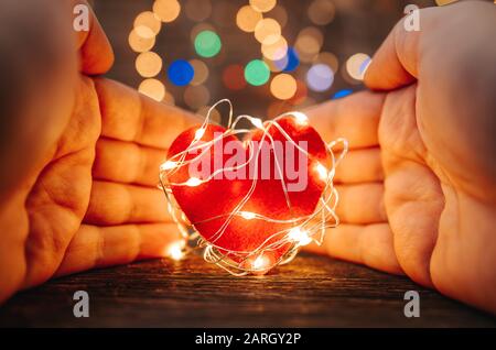 Holding a red heart shape covered with led lights on wooden and bokeh lights background. Valentines day and romance concept Stock Photo