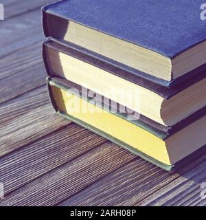 Three old books stacked in a pile on old wooden table, square frame Stock Photo