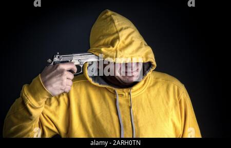 a man in a bright yellow hooded sweatshirt is about to attempt a suicide by gun Stock Photo