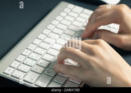 Girl works at home at the computer. Female hands are typing on the keyboard, close up. Stock Photo