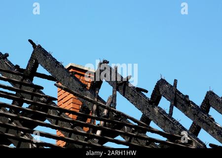 damaged exposed charred burnt black timber roof structure after house fire. fire damaged wood rafters. blue sky. fire safety and insurance concept.