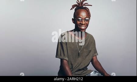 Smiling african man isolated on grey background looking at camera. Portrait of young man with dreadlocks tied together. Stock Photo