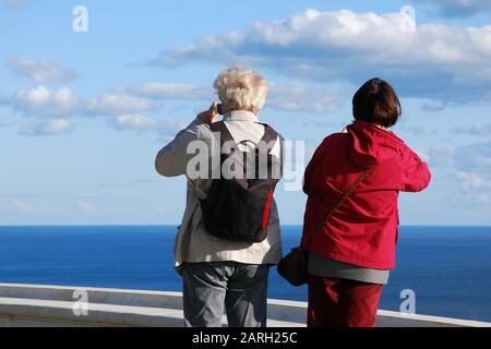 Senior couple travelling together, taking pictures of beautiful seascape with their mobile phones back view Stock Photo