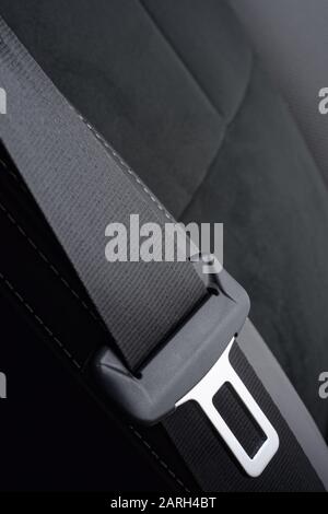 Car seat belt against dark grey leather seat. Black polyester webbing material seat belt and buckle. Stock Photo