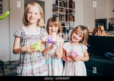 Three little sisters indoor at home playing with balloon looking camera smiling - happiness, having fun, family concept Stock Photo