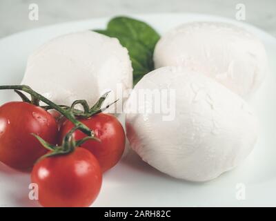 three mozzarella and cherry tomatoes on plate. White fresh cheese . Healthy dinner. Traditional italian ingredients Stock Photo