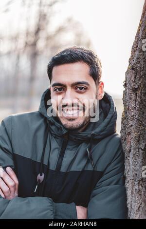 Portrait of beautiful young man looking a camera and sitting near a tree Stock Photo