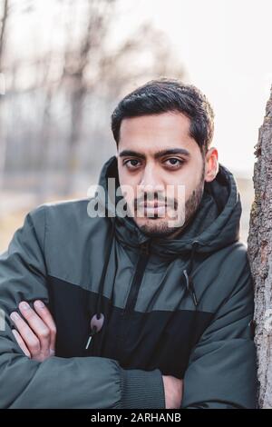 Portrait of beautiful young stylish man looking a camera and sitting near a tree in winter season Stock Photo