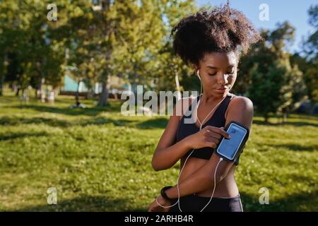 Close-up of an african american female runner athlete listening to music from smart phone in armband - young active black woman  Stock Photo