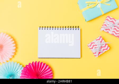 Empty notepad next to gift boxes and party decorations on bright yellow table, top view. Stock Photo