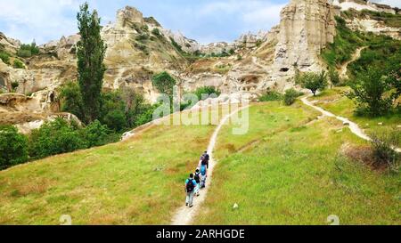 On a bright sunny day, a group of tourists walks along the rocky hills of Cappadocia in central Turkey. Photo taken from above using a drone. Stock Photo