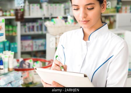 close up pharmacist with neutral emotions on face making notes in store Stock Photo