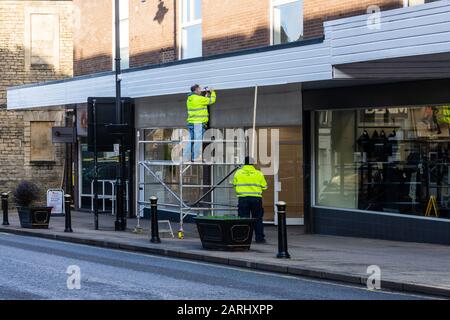 A workman on mobile scaffolding  using a hammer to fix a fascia board with his colleague below on the ground Stock Photo