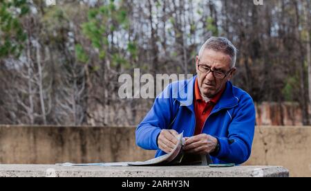 Old man with glasses reading the newspaper at park with the trees in the background Stock Photo