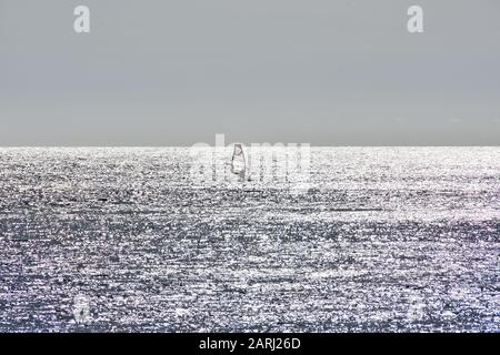 Windsurfer furrowing a silver sea by the reflections of the sun Stock Photo