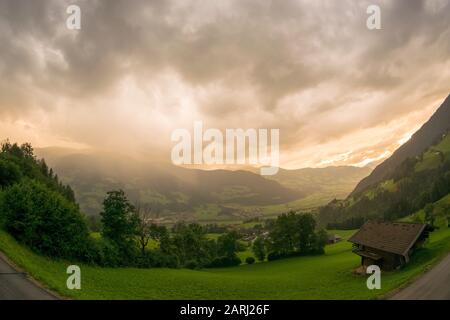 Rain and hail storm over a mountain landscape is illuminated by the setting sun Stock Photo