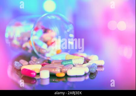 Assorted pills or capsules with medications on dark abstract background with reflection. Bold vibrant colors, futuristic purple, blue and turquoise li Stock Photo