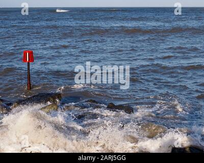 Waves breaking over rocks, red warning marker, Wales Stock Photo